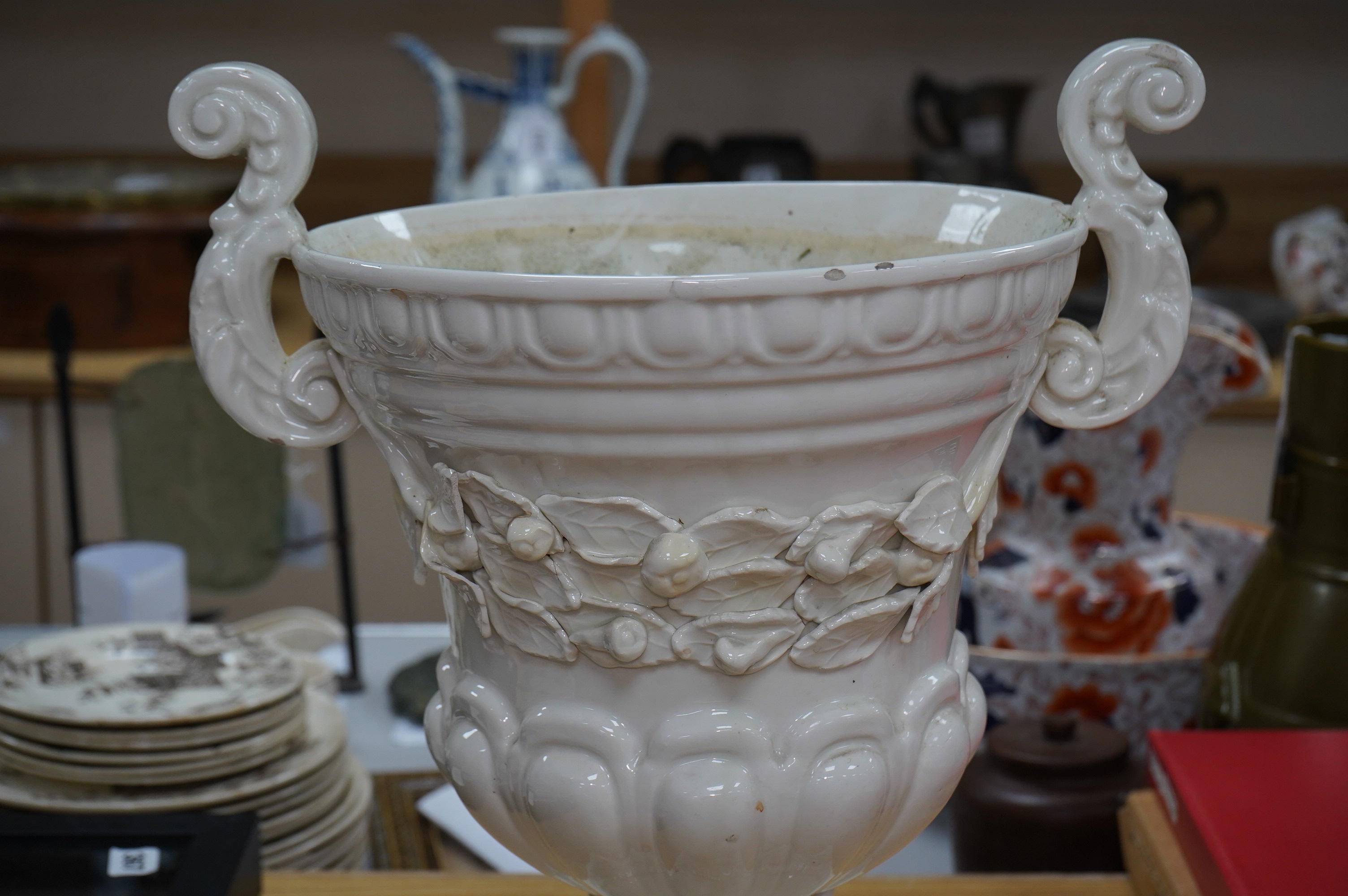 A large cream glazed pottery pedestal vase, with decorative swag of fruit and leaves, 43cm high. Condition - corner of square base broken, glazing chipped on top rim and fruit and leaf decoration broken